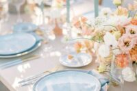 a refined pastel spring wedding table setting with pastel florals, dusty blue plates and candles, cutlery with blue handles