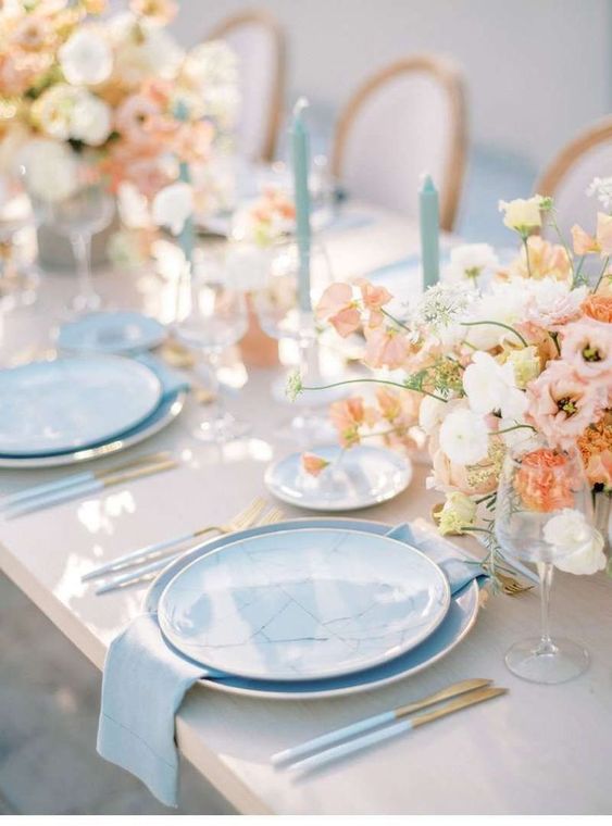 a refined pastel spring wedding table setting with pastel florals, dusty blue plates and candles, cutlery with blue handles