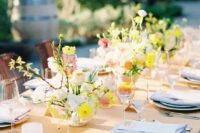 a refined spring wedding tablescape with a honey yellow tablecloth, bold yellow and neutral blooms, pink candles and blue napkins