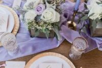 a refined spring wedding tablescape with a purple runner and candles, neutral and purple blooms and greenery, gold cutlery and gold rimmed glasses