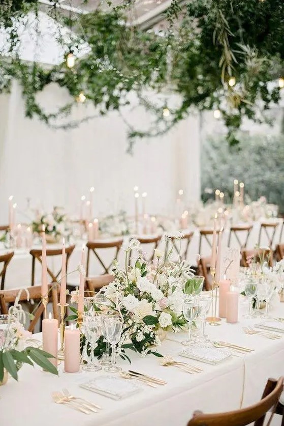 a romantic blush and ivory wedding tablescape with neutral blooms, blush candles, gold cutlery and neutral menus