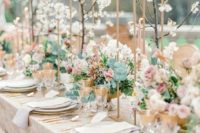 a romantic pastel spring wedding reception with a lace tablecloth, blush blooms and cherry blossom over the table
