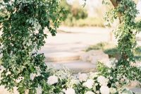 a round wedding arch covered with greenery and white blooms is an airy and chic idea for a spring or summer wedding