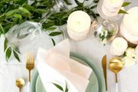 a simple and fresh spring wedding table with greenery, brich bark wrapped candles, green plates and gold and white cutlery