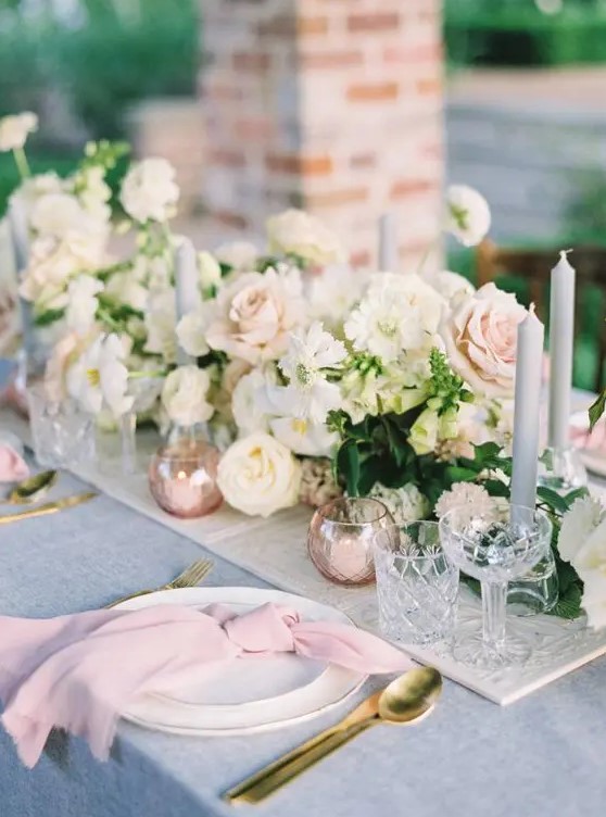 a sophisticated spring wedding tablescape with a blue tablecloth and pink napkins, neutral and blush blooms and grey candles
