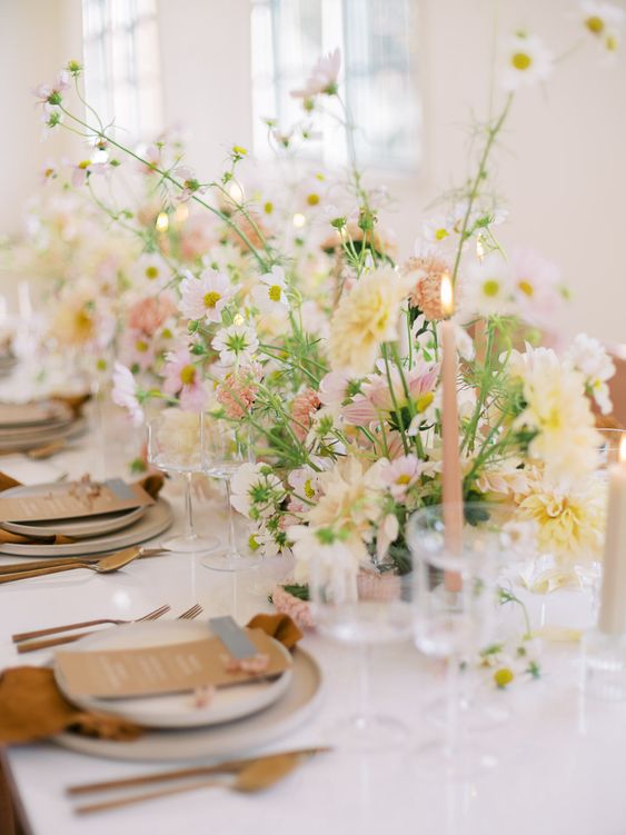 a sophisticated spring wedding tablescape with white, blush and yellow blooms, pink candles, rust-colored napkins