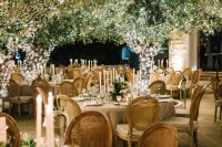 a sophisticated wedding reception space with greenery and lights, with neutral linens, tall and thin candles and greenery on the tables