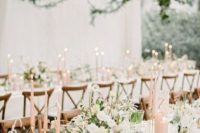 a spring wedding reception with greenery over the tables, blush candles, white blooms and greenery on the tables and gold touches
