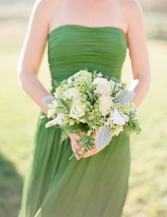 a strapless green bridesmaid dress with a draped bodice and a pleated skirt plus a greenery and white bloom wedding bouquet