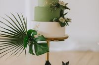 a stylish green and white wedding cake with gold leaf and tropical leaves around for a tropical wedding