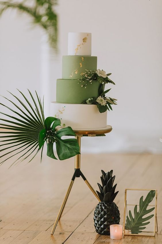 a stylish green and white wedding cake with gold leaf and tropical leaves around for a tropical wedding