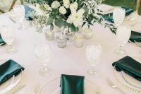 a stylish wedding table setting in white accented with emerald napkins and with a green and white wedding centerpiece with thistles