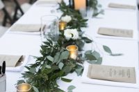 a stylish wedding tablescape with a greenery runner, candles and candle lanterns, neutral menus and white linens