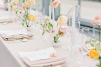 a subtle wedding tablescape with a blush tablecloth and napkins, pastel blooms, white candles and white menus