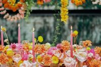 a super colorful wedding reception with yellow, orange and hot pink blooms, a hot pink tablecloth and candles and flower garlands over the table
