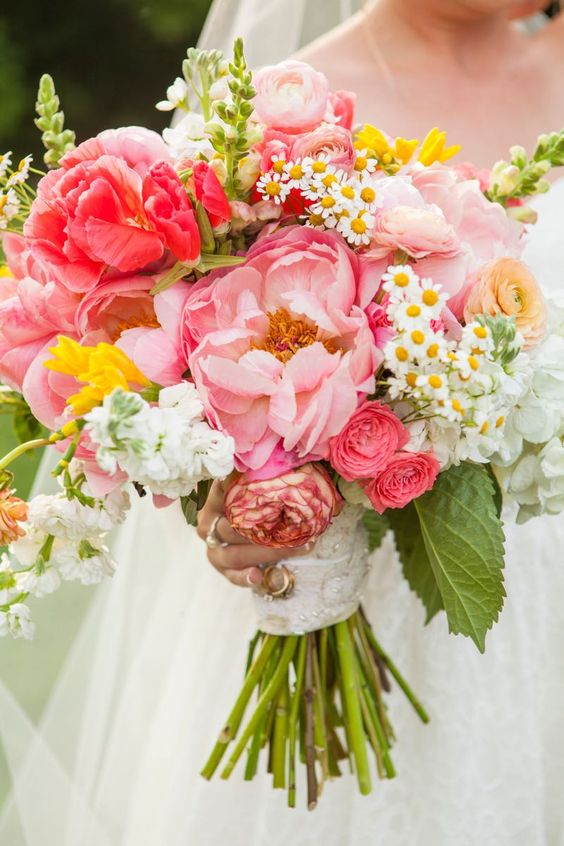 a super lush and bold wedding bouquet of pink peonies, chamomiles, yellow blooms and some foliage is wow
