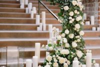 a wedding staircase decorated with greenery and white roses plus pillar candles and candle lanterns is a very chic idea