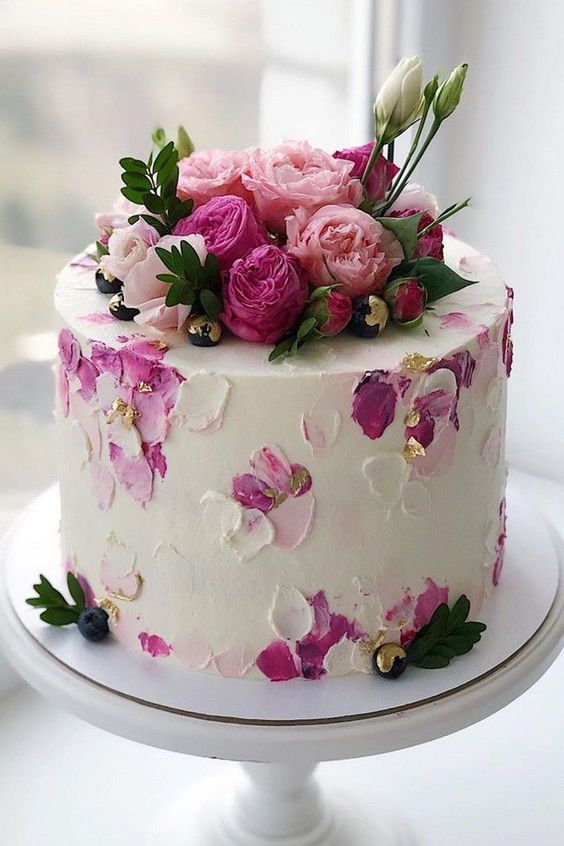 a white wedding cake with dimensional hand painted blooms and petals, with gold leaf and bold fresh blooms on top