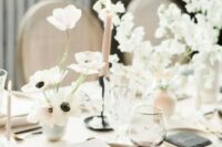 an airy neutral wedding table setting with neutral linens, elegant plates, blush tall and thin candles, white blooms and black and godl cutlery