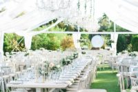 an all-white spring wedding reception with greenery, pastel blooms and white chandeliers on greenery ropes