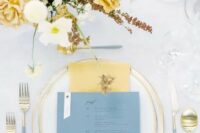 an elegant and airy wedding tablescape with gold edge porcelain and cutlery with grey handles, yellow napkins and a yellow floral arrangement