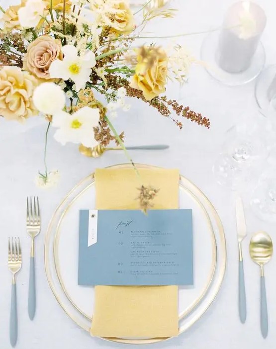 an elegant and airy wedding tablescape with gold edge porcelain and cutlery with grey handles, yellow napkins and a yellow floral arrangement