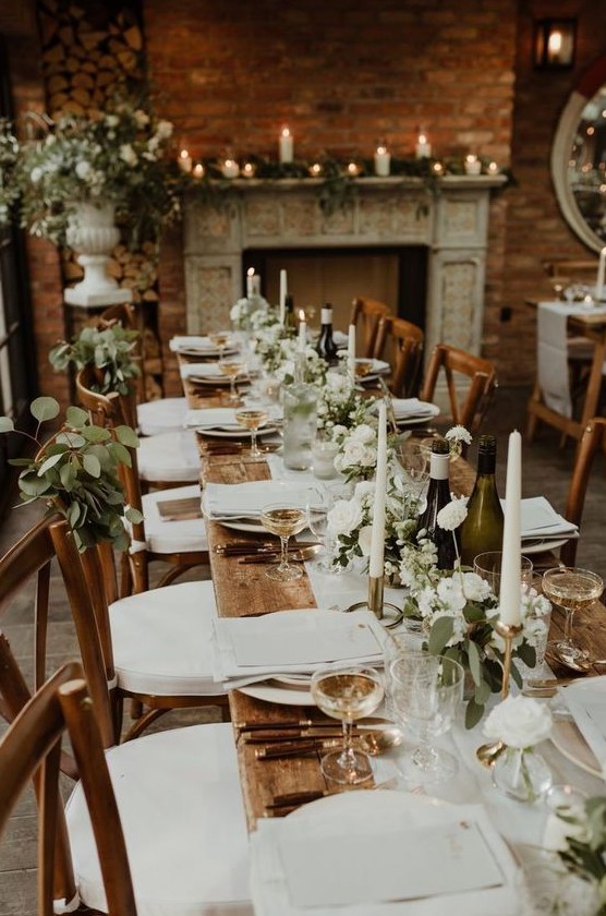 an elegant barn wedding tablescape with an uncovered table, white linens, a greenery and white bloom table runner