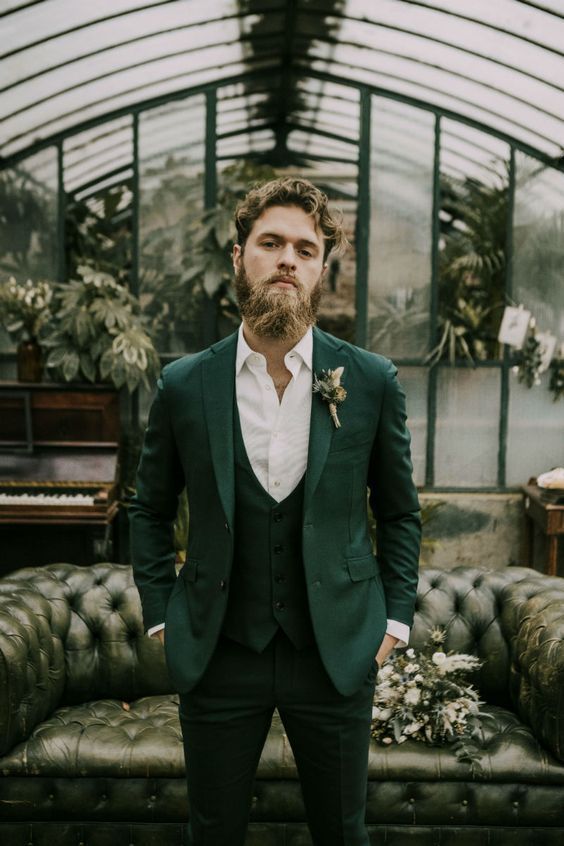 an elegant groom wearing a green three-piece suit, a white shirt and a green and white boutonniere looks chic