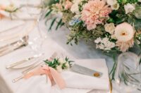 an elegant wedding tablescape with pastel and neutral blooms and greenery, gold-rimmed plates and silver cutlery plus neutral linens