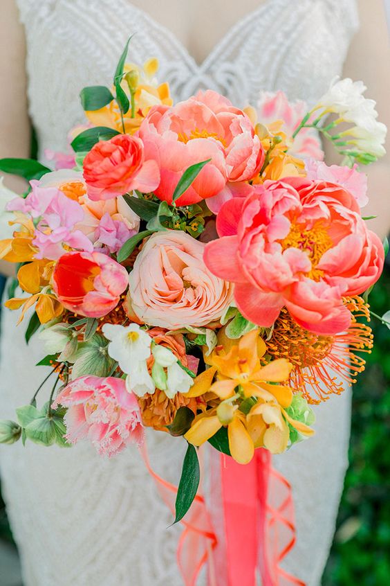 an incredibly bright wedding bouquet of coral, pink, light pink and yellow blooms, greenery and bold ribbons
