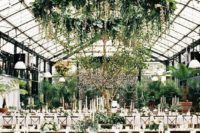 an indoor spring wedding reception with greenery chandeliers, greenery arrangements, trees in pots and candles
