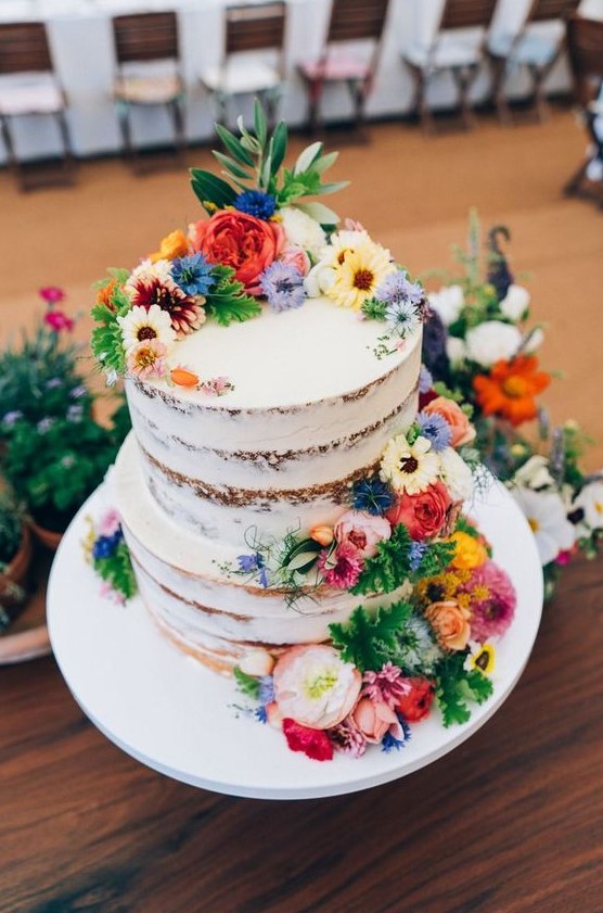 a bright semi naked summer wedding cake with colorful blooms and greenery is an awesome piece