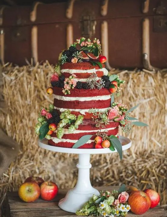 a delicious naked red velvet wedding cake decorated with pink blooms, greenery, mini apples and blackberries is amazing for a summer or fall wedding