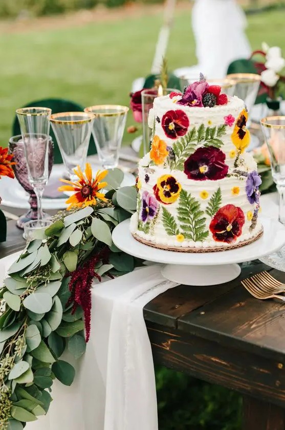 a white buttercream wedding cake with pressed super bold red, yellow and purple blooms and leaves is a gorgeous idea for a summer wedding