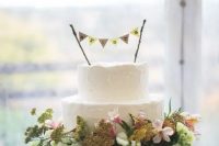 113 a white textural buttercream wedding cake topped with a banner, on a wood slice with greenery and blooms
