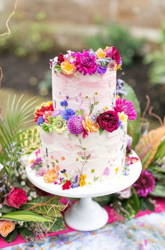 a white textural wedding cake with pink brushstrokes and super bold fresh blooms in all the shades of rainbow