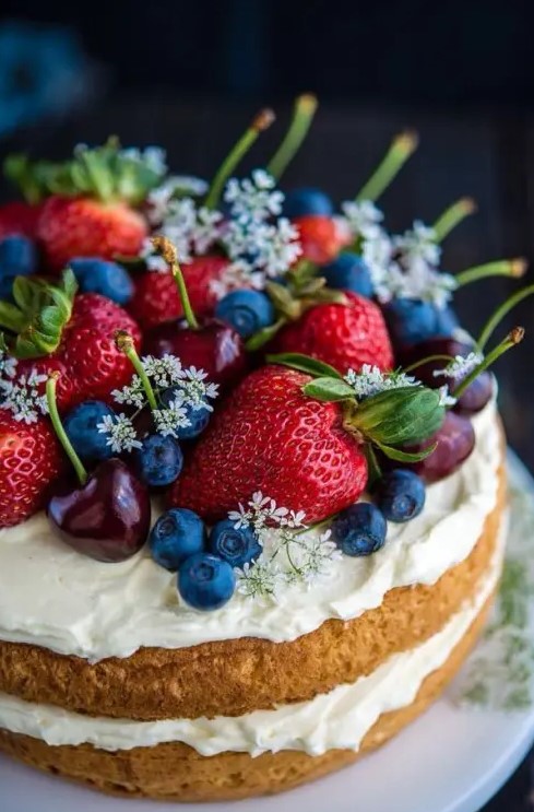 a one tier naked wedding cake topped with whipped cream with fresh berries, greenery and blooms is a beautiful and cool idea for a summer wedding