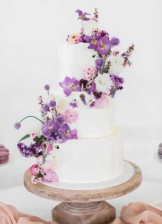 a white wedding cake that received a touch of color with white, pink and purple blooms looks lovely and such decor can be easily added or removed
