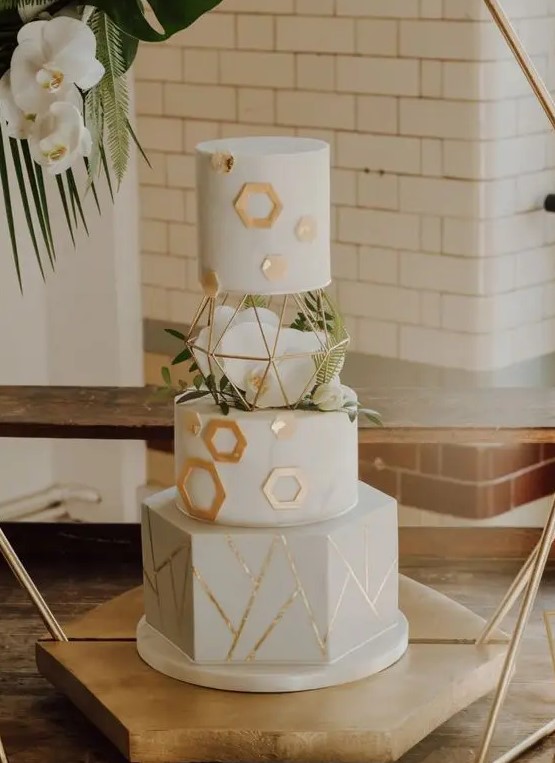 a white wedding cake with gold hexagons and geometric patterns, white orchids and greenery is a chic and refined idea