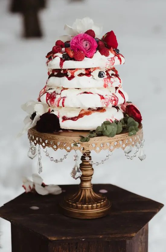 a gorgeous pavlova wedding cake topped with fresh berries and berry sauce, with pink, red and white blooms plus eucalyptus for a refined wedding