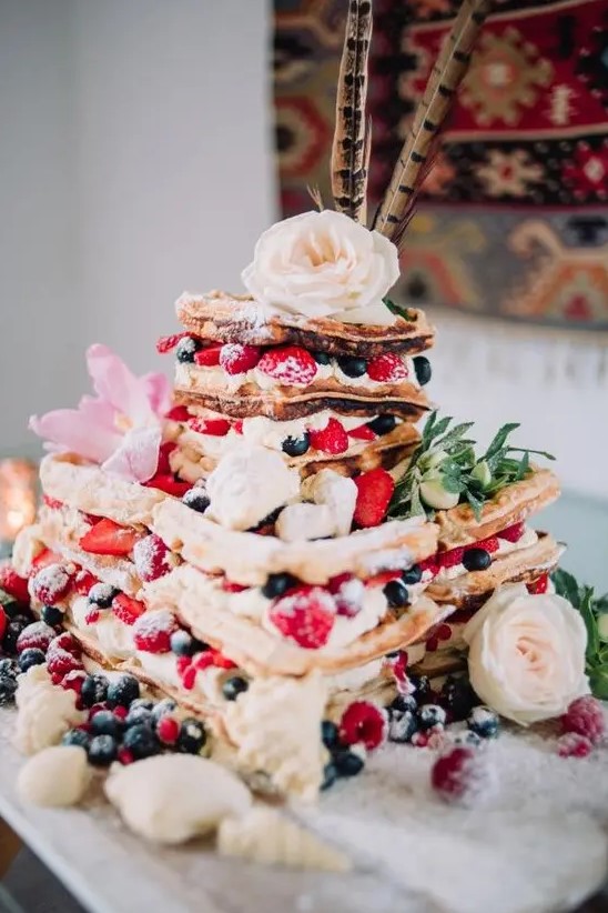 a gorgeous summer boho wedding cake with fresh berries, pink and white blooms, greenery and feathers on top