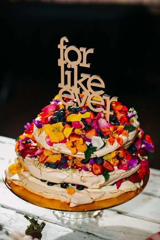 a pavlova wedding cake with colorful petals, bright berries and a letter topper is a lovely idea for a bright boho wedding
