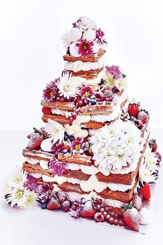 an oversized waffle wedding cake with various types of berries, white and pink blooms and some meringues