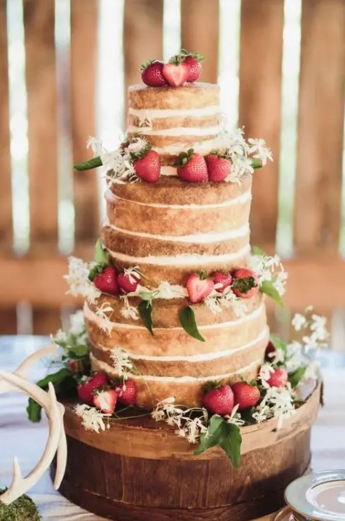 a naked wedding cake topped with fresh strawberries and white blooms and greenery is a cool rustic summer wedding piece