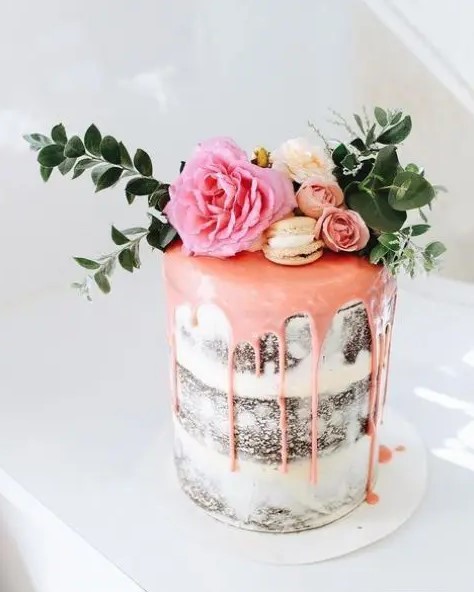 a small chocolate naked wedding cake with pink drip, pink and neutral blooms, macarons and greenery is delicious