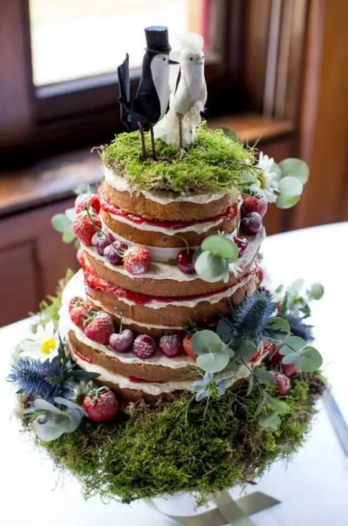 a summer woodland naked wedding cake with fresh berries, moss, greenery, bird toppers on a moss pillow with greenery