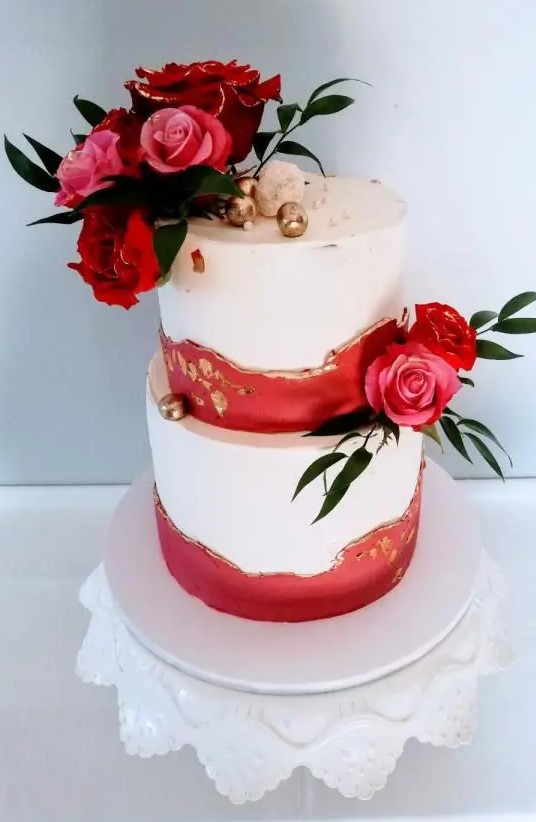 a beautiful and chic wedding cake done with red and gold leaf textural touches, pink and red roses and greeenery, gilded cherries on top