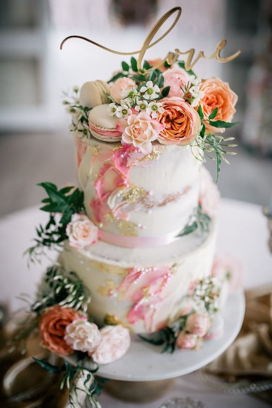 a beautiful spring or summer two-tier wedding cake with bright watercolors, gold, pearls, fresh blooms and greenery and a calligraphy topper