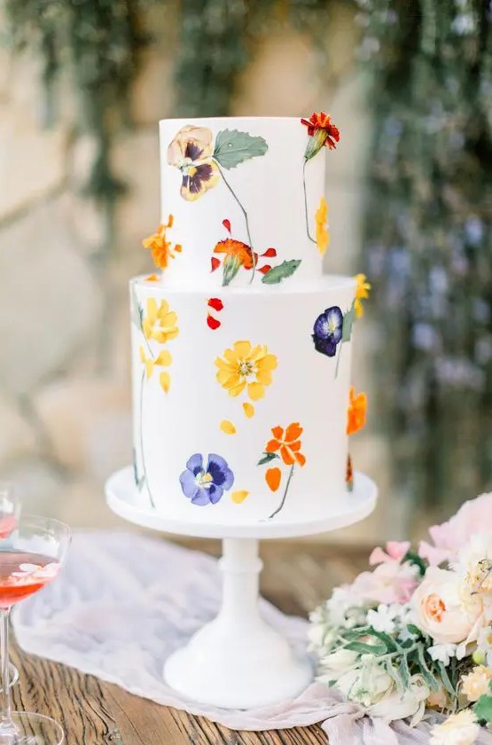 a bold white buttercream wedding cake with colorful pressed flowers and leaves is amazing for a spring or summer wedding