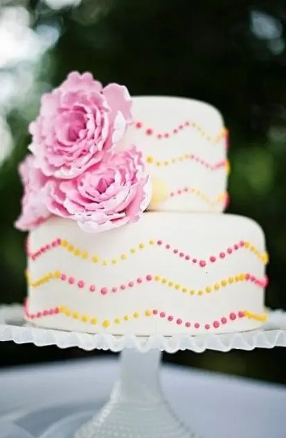 a bright summer wedding cake with pink and yellow chevron polka dot patterns and pink sugar blooms is a gorgeous idea to rock